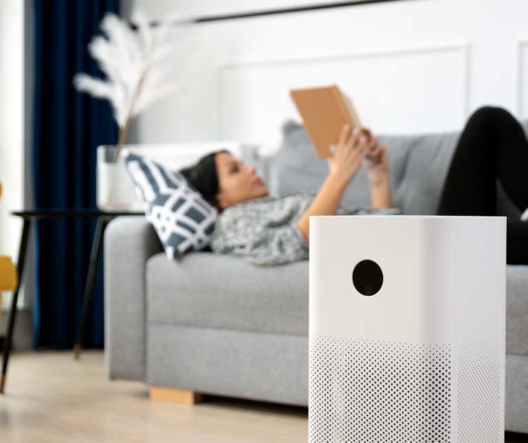 Woman laying on the couch reading with an air purifier in front of her