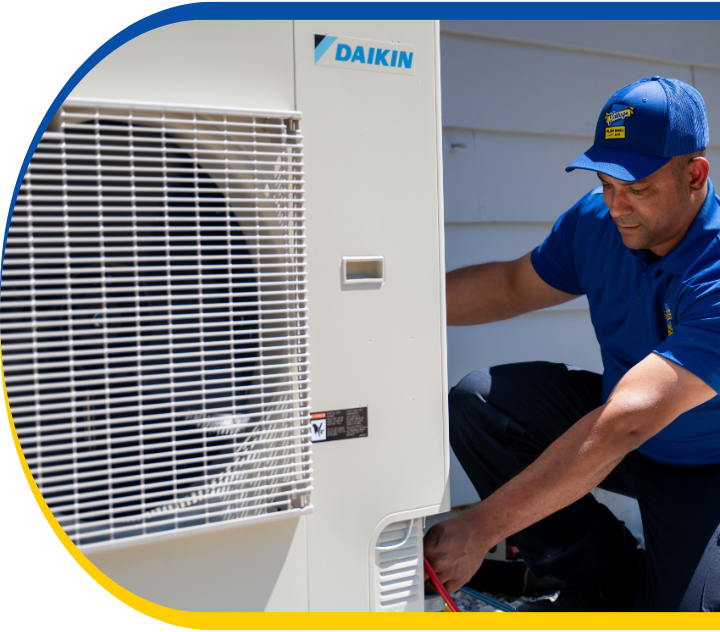 Technician in a blue uniform inspecting an air conditioning unit outdoors.